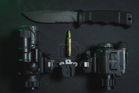 Tactical knife with a fixed blade, night vision binocular and 5.56x45mm cartridge. 