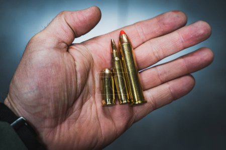 Cartouches de différents calibres provenant d'armes à feu dans la main d'un homme, photo rapprochée. 