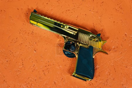 Pistol Desert eagle 50AE gold color against an orange wall. 
