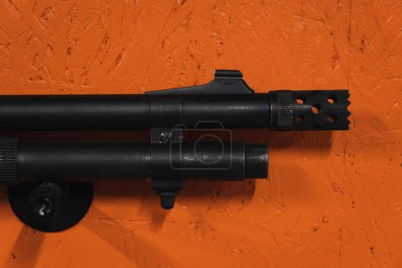 A shotgun barrel with a muzzle brake against the background of an orange wall. 