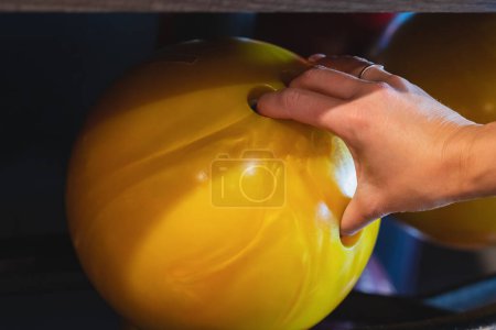 Foto de La mano de una mujer toma una bola de bolos amarilla, foto de cerca. - Imagen libre de derechos