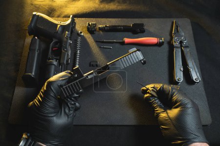 Reinigen und Reparieren von Waffen. Hände eines Büchsenmachers und eine zerlegte Pistole G19 in einer Werkstatt. 