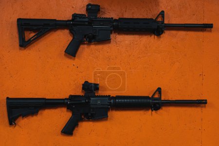 Téléchargez les photos : Deux fusils M4A1 déchargés sur un mur orange dans un champ de tir. - en image libre de droit