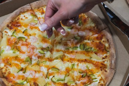 Die Hand einer Frau greift nach einer Pizza, Nahaufnahme Foto. 