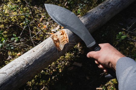 A large black tactical kukri knife for chopping wood in a man's hand in the forest.