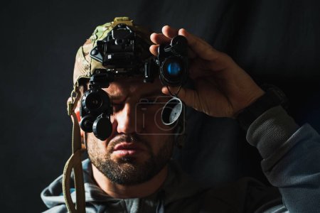Téléchargez les photos : Portrait d'un militaire barbu avec un dispositif binoculaire de vision nocturne sur la tête. Photo mise au point douce. - en image libre de droit