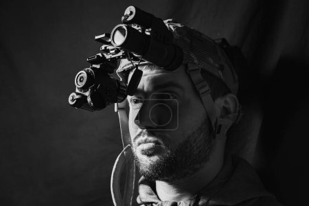 Portrait of a military man with a beard with a binocular night vision device on his head. Black and white photo. 