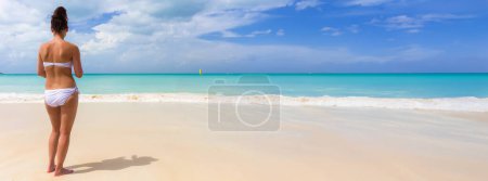 Foto de Hermosa mujer en bikini blanco de pie frente a la playa isla tropical con nubes y velero - Imagen libre de derechos