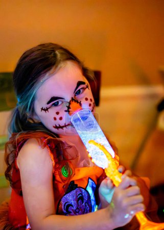 Téléchargez les photos : Potion à boire pour enfants sur l'épouvantail d'Halloween maquillage visage peinture luisant dans la lumière noire - en image libre de droit