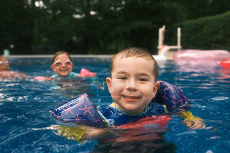 Téléchargez les photos : Jeune garçon profiter de la piscine avec des nageurs - en image libre de droit