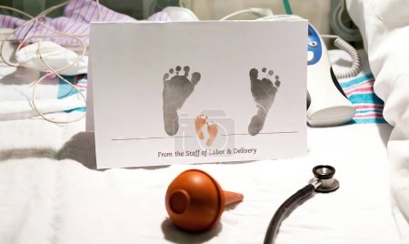 Foto de Huellas de bebé recién nacido en la tarjeta del hospital con estetoscopio y bombilla de succión - Imagen libre de derechos