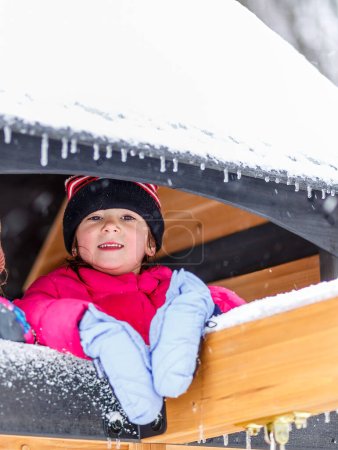 Photo for Young girl child under icy snow covered play house roof with icicles during cold winter day - Royalty Free Image