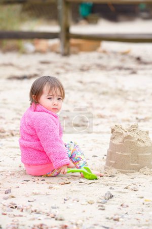Téléchargez les photos : Aventure sur la plage des jeunes enfants : construire des châteaux de sable par une journée fraîche - en image libre de droit
