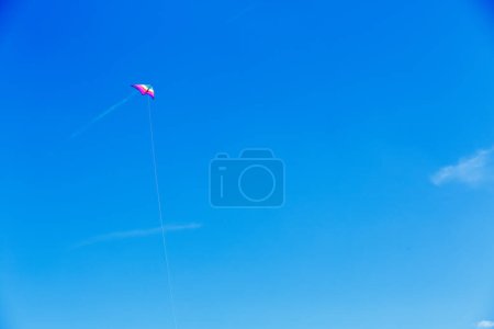 Téléchargez les photos : Cerf-volant classique traditionnel arc-en-ciel coloré avec nuage contrail et ciel bleu dans un paysage minimaliste - en image libre de droit