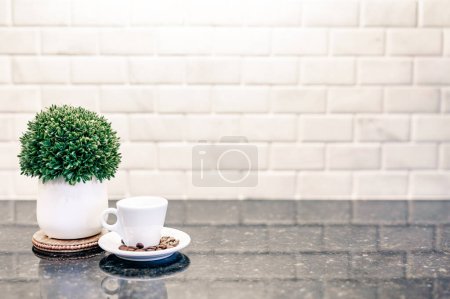 Foto de Taza de café expreso y platillo con granos de café tostados oscuros con contador moderno y reflexión de azulejos del metro blanco en la cocina bar cafetería con planta verde - Imagen libre de derechos