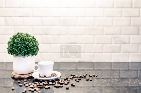 Foto de Taza de café expreso y platillo con granos de café tostados oscuros con contador moderno y reflexión de azulejos del metro blanco en la cocina bar cafetería con planta verde - Imagen libre de derechos