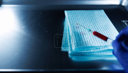 Foto de Primer plano de una aguja hipodérmica con una gota de sangre en la punta que se sostiene sobre una bandeja médica - Imagen libre de derechos