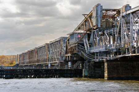 Téléchargez les photos : Drapeau américain ornant un grand pont métallique sur l'eau avec un ciel gris nuageux - en image libre de droit