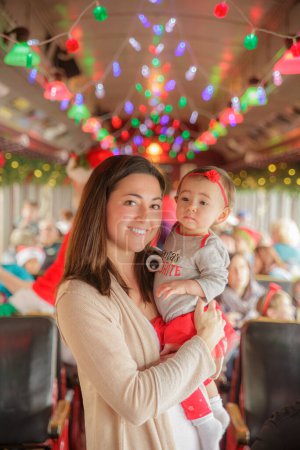 Foto de Madre sosteniendo hermosa niña con luces de Navidad de colores en el fondo en el autobús del tren - Imagen libre de derechos