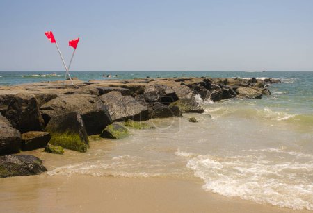 Téléchargez les photos : Drapeaux rouges sur Ocean Rock Jetty, La sécurité au milieu des vagues - en image libre de droit