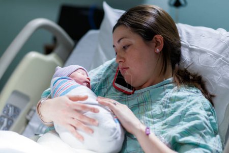 Foto de Madre y su bebé recién nacido en una sala de maternidad del hospital mientras mamá habla por su teléfono celular - Imagen libre de derechos