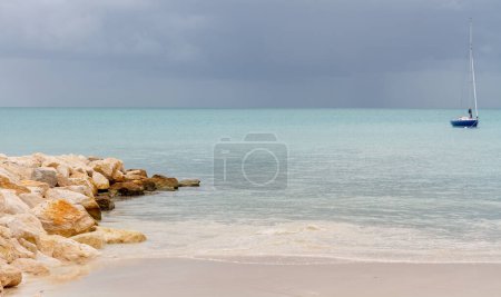 Foto de Antigua playa y embarcadero de roca con barco de vela y nubes de tormenta en el mar tranquilo - Imagen libre de derechos