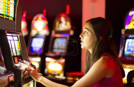 Photo for Young adult brunette woman sitting and playing slot machine at casino - Royalty Free Image