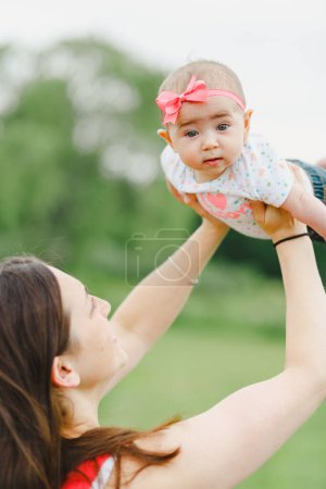 Téléchargez les photos : Jeune femme adulte levant les yeux et tenant bébé fille avec enfant regardant la caméra - en image libre de droit