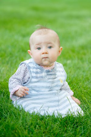 Téléchargez les photos : Portrait de bébé assis debout dans l'herbe avec fond Bokeh - en image libre de droit