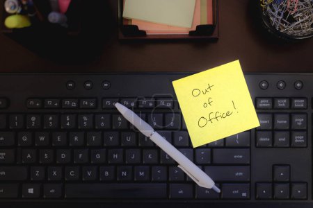 Sticky Note on Office Desk Saying "Out of Office"
