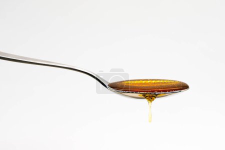 Primer plano de la miel vertiendo en la cuchara con gotas contra el fondo blanco