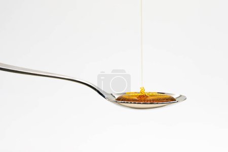 Primer plano de la miel vertiendo en la cuchara con gotas contra el fondo blanco