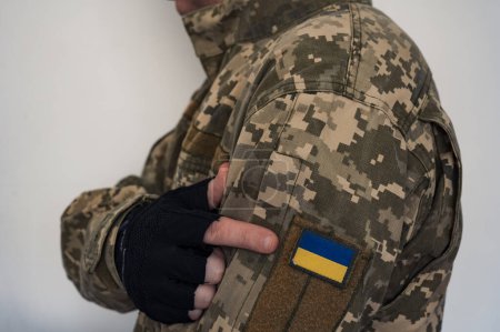 Photo for Arm in glove of ukrainian soldier in uniform point to a banner of the Ukrainian flag on a military camouflage suit. Pixeled digital soldier's pixel camouflage uniform with ukrainian flag on chevron in blue and yellow colors. - Royalty Free Image