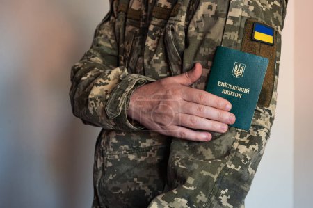 Soldat im Taktikanzug hält Militärausweis neben Fahne. Ukrainische Pixeluniform