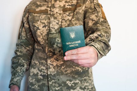 Soldier in camouflage holds military identity card in left hand. Ukrainian pixel uniform