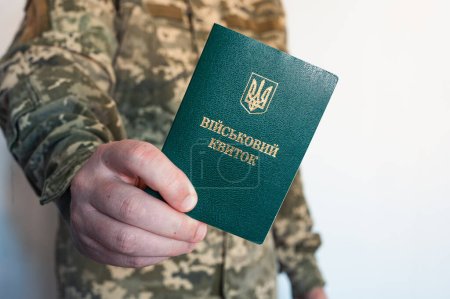 Photo for Soldier in camouflage holds green military id doc book in right hand. Ukrainian pixel - Royalty Free Image