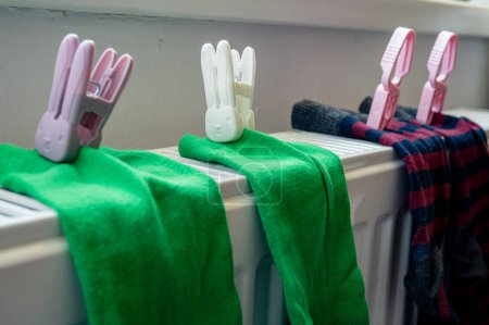 Photo for Two pairs of colored socks with clothespin on the white radiator after washing. Housing, economy, domestic theme - Royalty Free Image