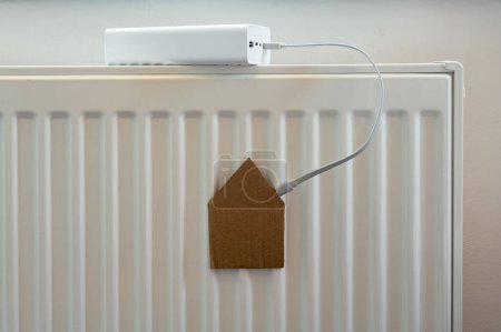 Photo for White power bank charges paper house on the radiator. Housing, energy, economy, domestic theme - Royalty Free Image