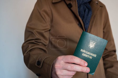 Translation: "military id". Man in coat holds army document for rookie, veteran, soldier in hand on white background