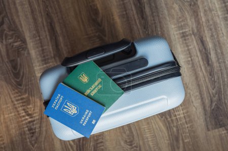 Photo for Translation: "military id". Travel blue suitcase stands on wooden floor with ukrainian passport and mil document for soldiers and civils on it - Royalty Free Image