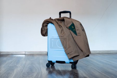 Photo for Translation: "military id". Travel bag with open handle and coat stands on floor. In pocket there is document - Royalty Free Image