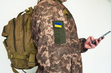 Soldado ucraniano en uniforme militar pixel con mochila táctica y smartphone en la mano