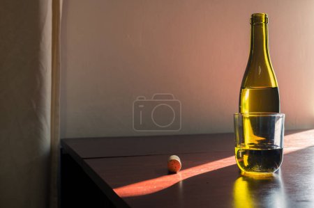 Photo for White glass and opened green bottle of wine with cork on table in sunl ray. Classic winery cellar beautiful image - Royalty Free Image