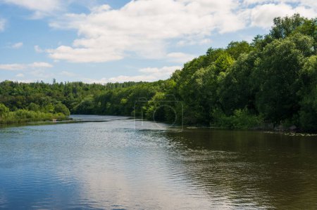 Calm river with lush green forest on banks. Blue sunny sky white clouds. Ecology pure nature