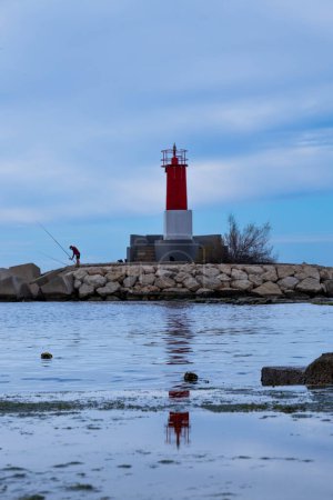 Fisherman in a lighthouse reflected in the sea