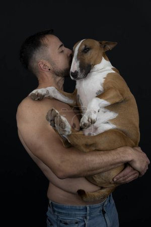 Photo for Strong shirtless man on black background kissing his dog - Royalty Free Image