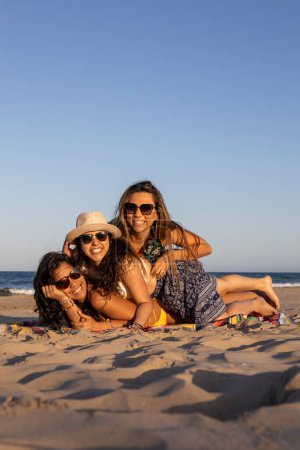 Drei Mädchen lächeln und spielen auf einem Handtuch am Strand