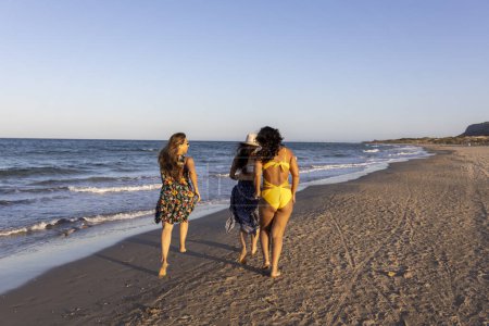 Three girls with their backs to themselves running along the sea