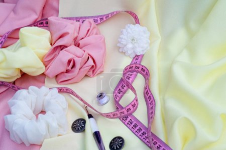Photo for Yellow, pink, white scrunchies, one white flower, pink measuring tape, two buttons on pink and  yellow textile. Place for text, logo. Handmade, fashion - Royalty Free Image