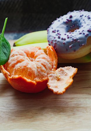 one glazed violet donut, mint, peeled fresh juicy mandarin and bananas on wooden board. Healthy food concept